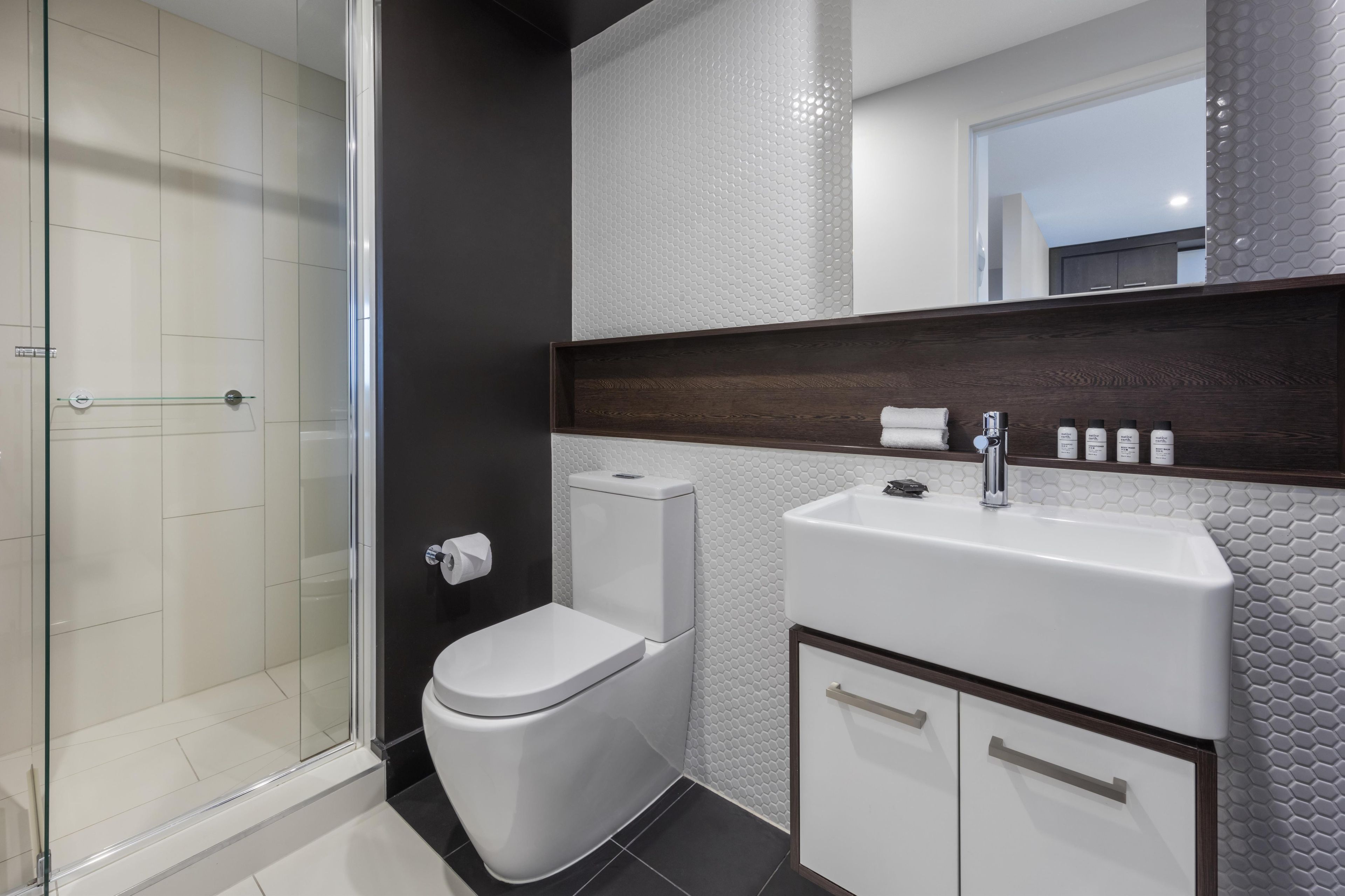 A modern bathroom with a glass shower enclosure, a white toilet, a sink with a mirror above, and a cabinet below.