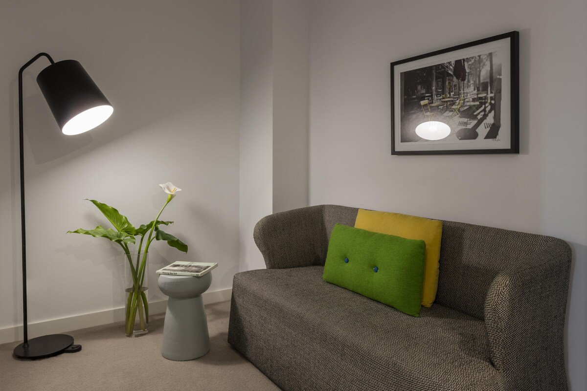 Une pièce avec un canapé, une lampe sur pied, un tableau encadré au mur et une plante en pot.