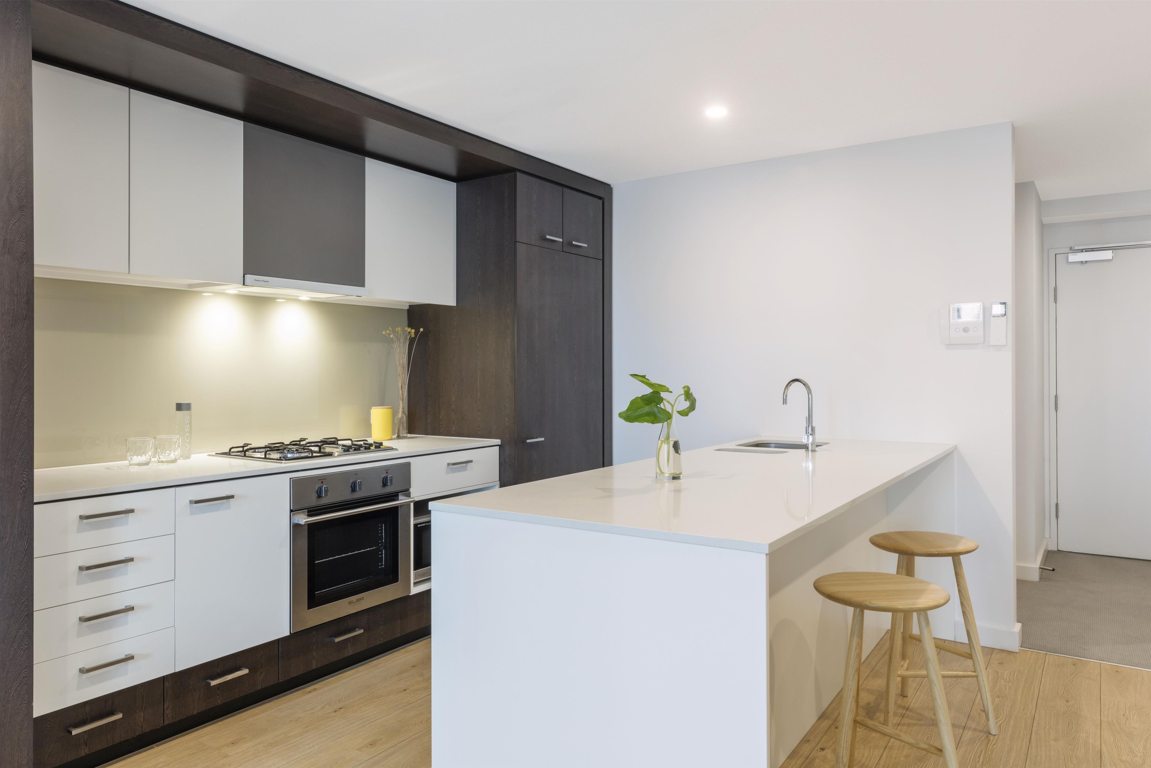 Una cocina moderna con armarios blancos, una isla central con taburetes, una estufa a gas y un fregadero.