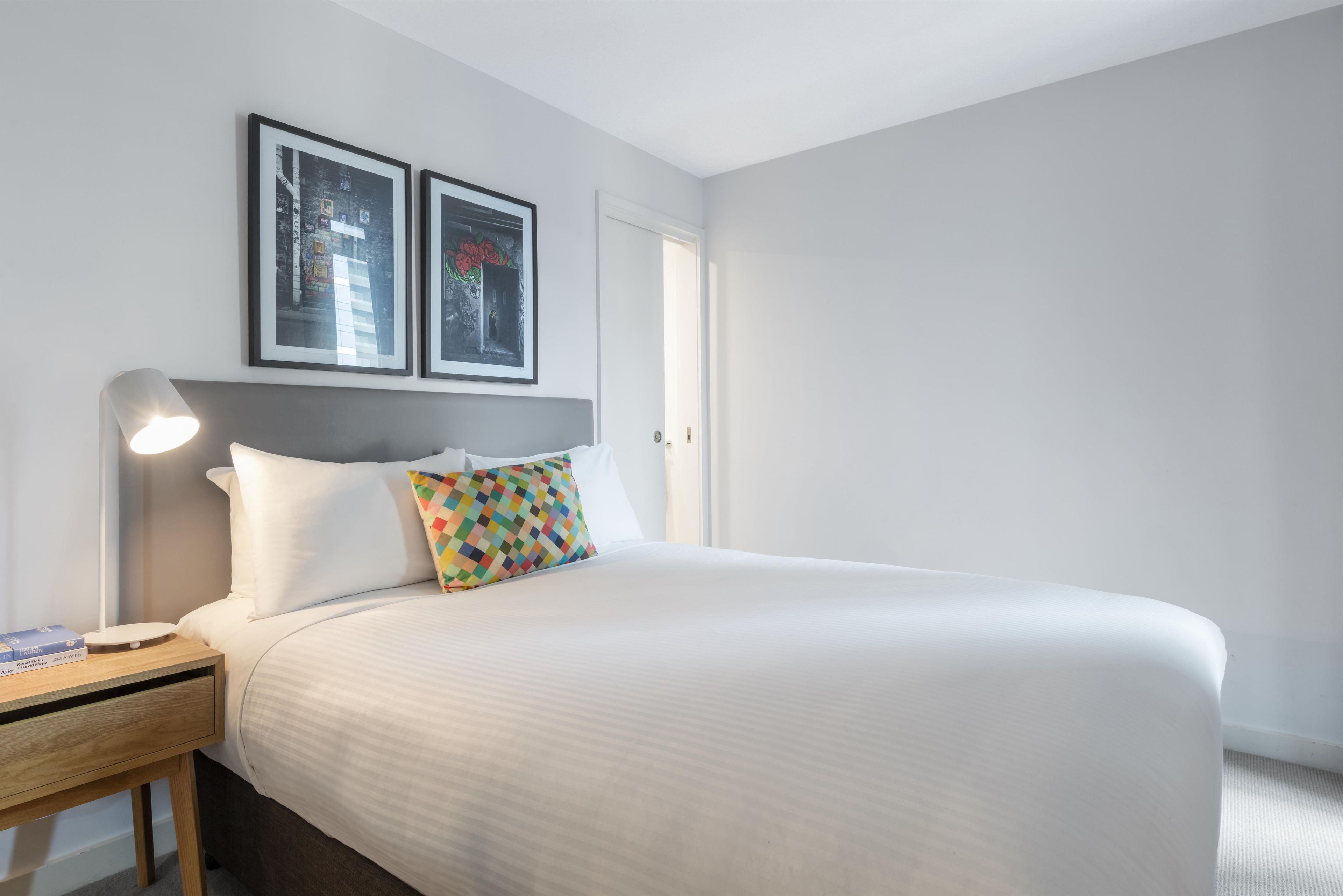 A hotel room with a bed, a bedside table with a lamp, and two framed pictures on the wall.