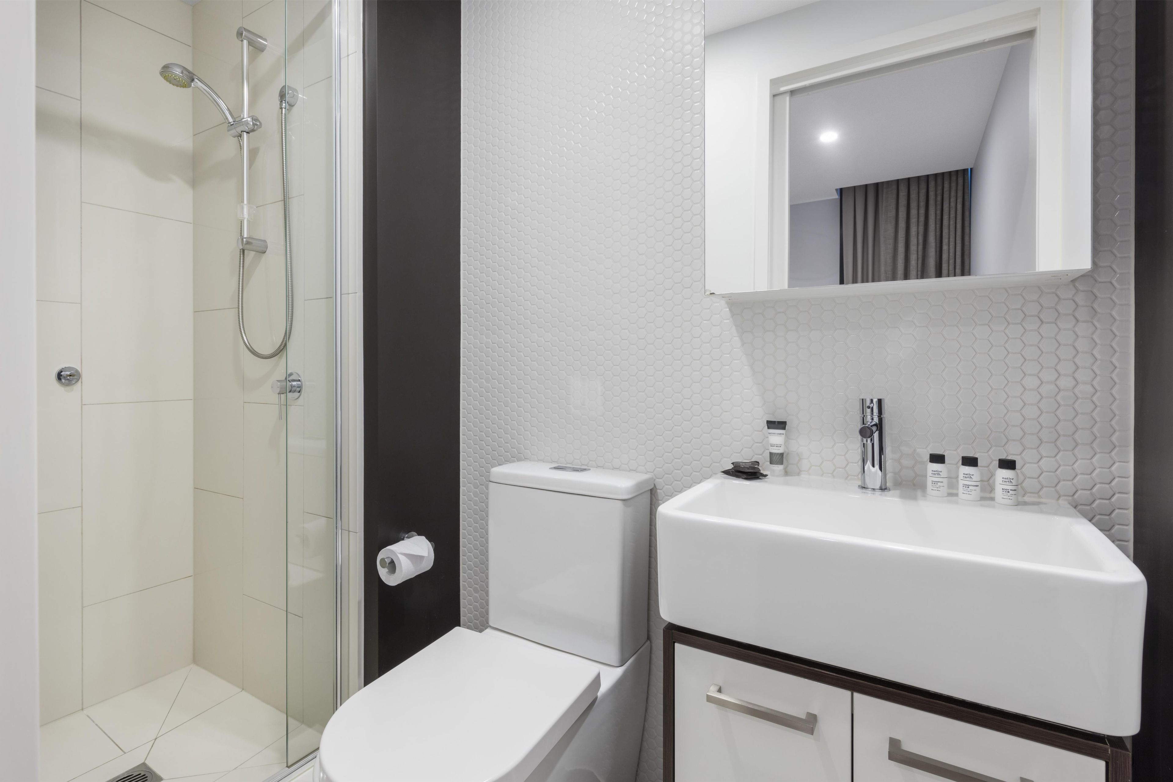 Een badkamer met een douchecabine van glas, een wit toilet, een wastafel met toiletartikelen en een spiegel erboven.