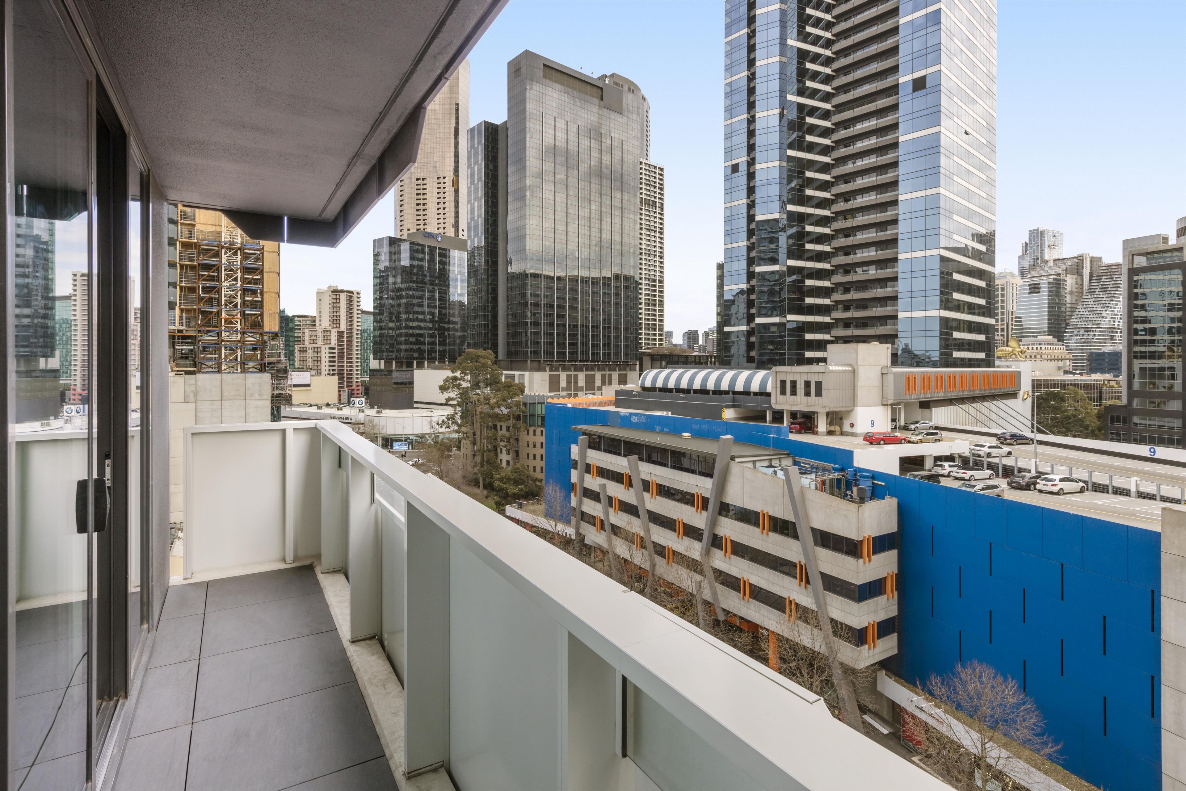 A balcony with a city view, a parking garage, and modern buildings.