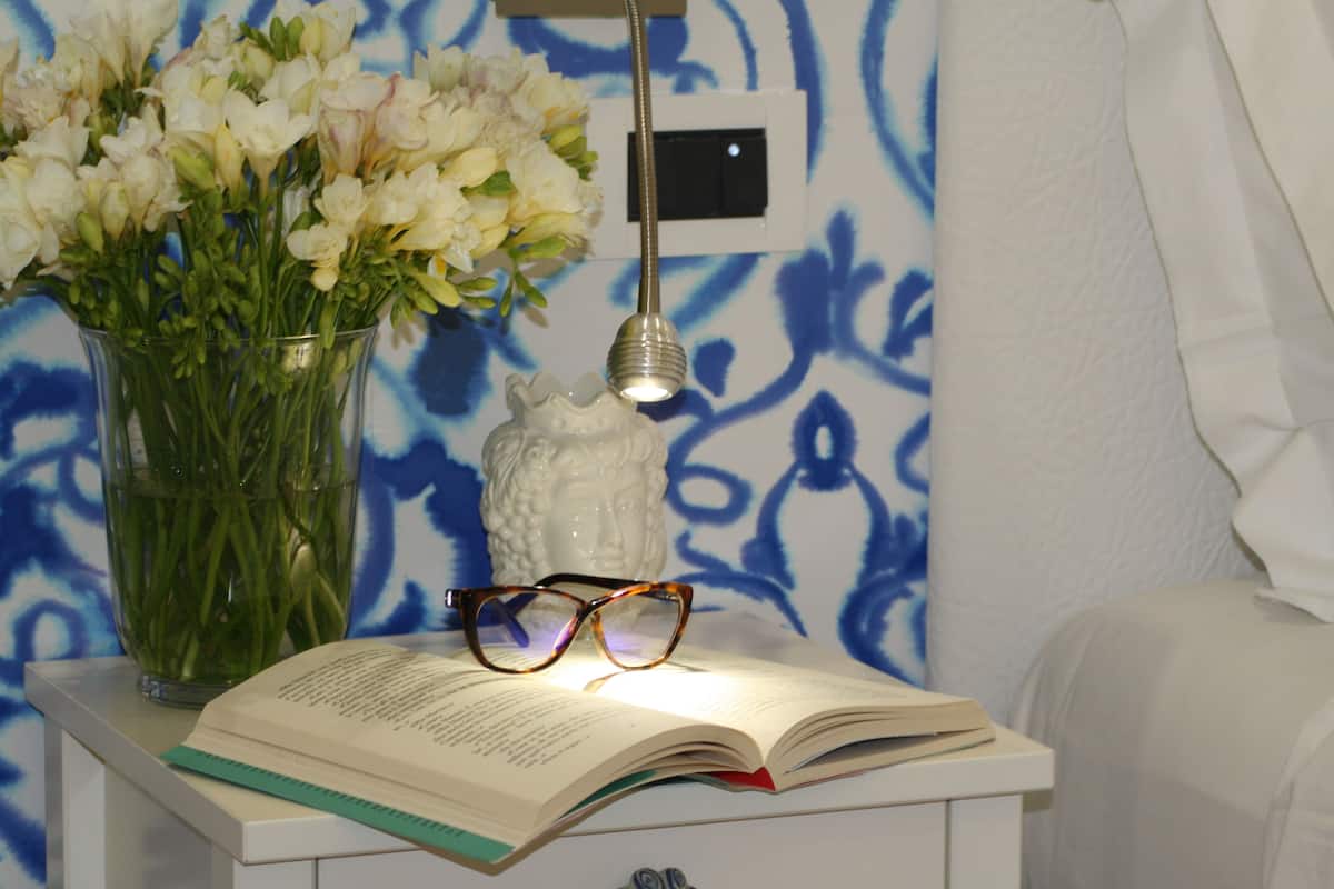 A bedside table with a book, a pair of glasses, and a vase of flowers.