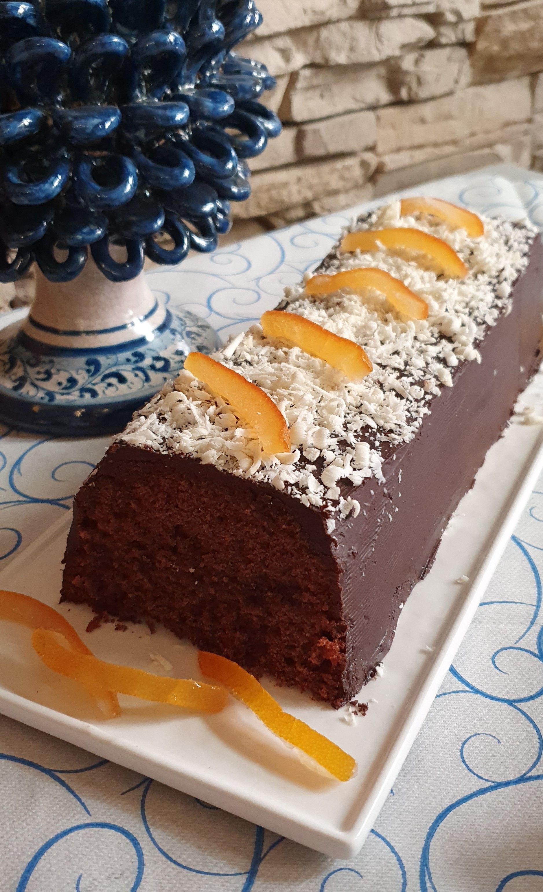 Ein rechteckiger Schokoladenkuchen mit Orangenscheiben und Kokosraspeln auf einem weißen Teller.