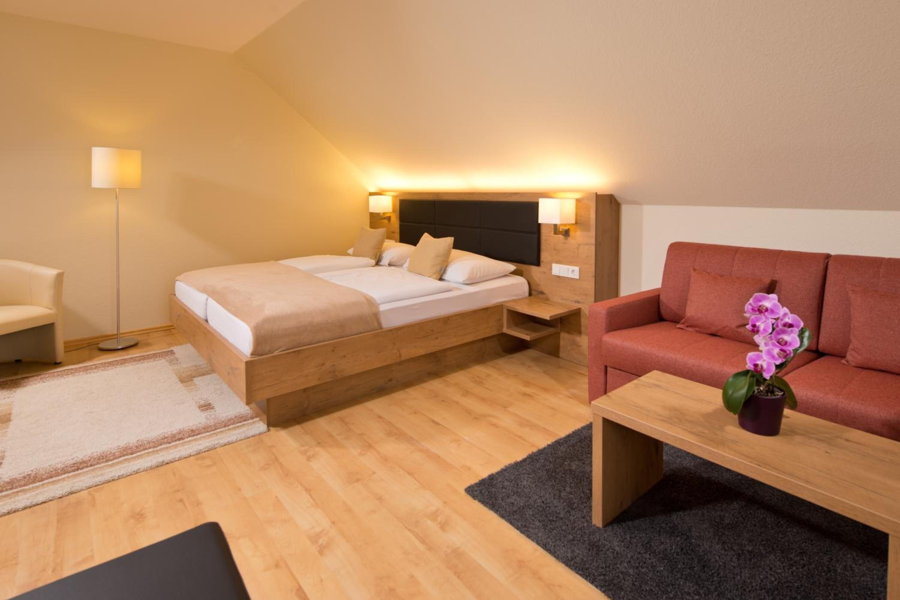 Une chambre d’hôtel moderne avec un lit en bois, un canapé, une petite table et une lampe sur pied.