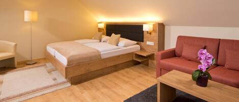 Une chambre d’hôtel moderne avec un lit en bois, un canapé, une petite table et une lampe sur pied.
