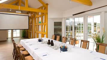 Un salón de conferencias con una larga mesa, sillas, una pantalla de proyector y vistas a través de puertas de vidrio.