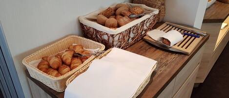 Un bufé de desayuno con cruasanes, panecillos y una bandeja con un perro caliente y cubiertos.