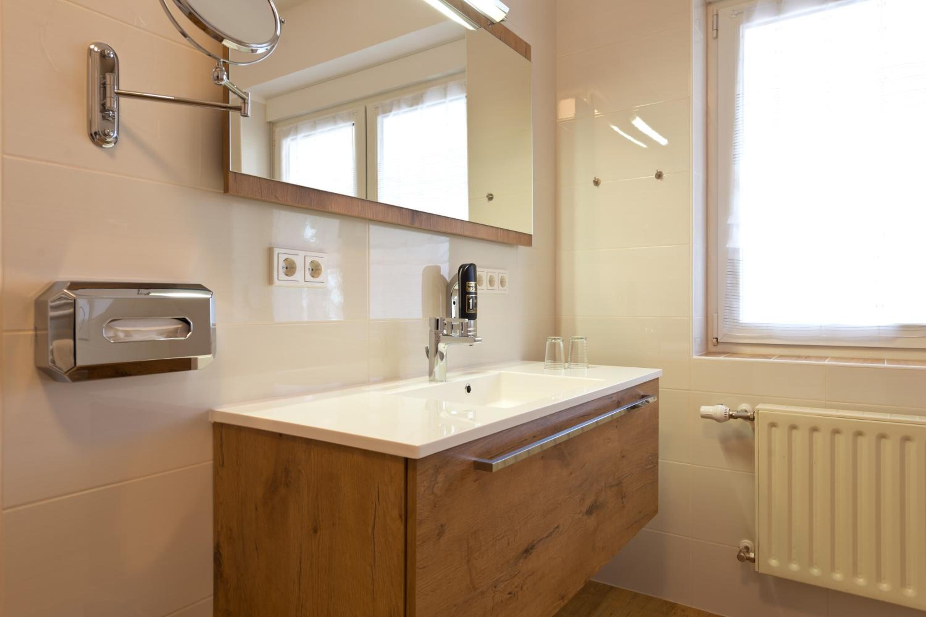 Ein modernes Badezimmer mit einem Holzwaschtisch, einem weißen Waschbecken, einem Spiegel und einem Fenster für natürliches Licht.