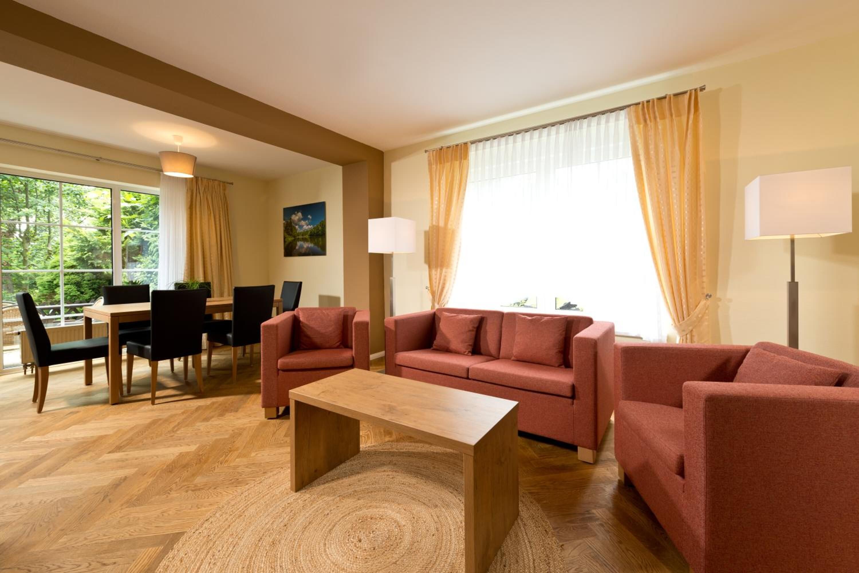 Een moderne woonkamer met een houten vloer, een zithoek, een eettafel met stoelen en een groot raam met gordijnen.