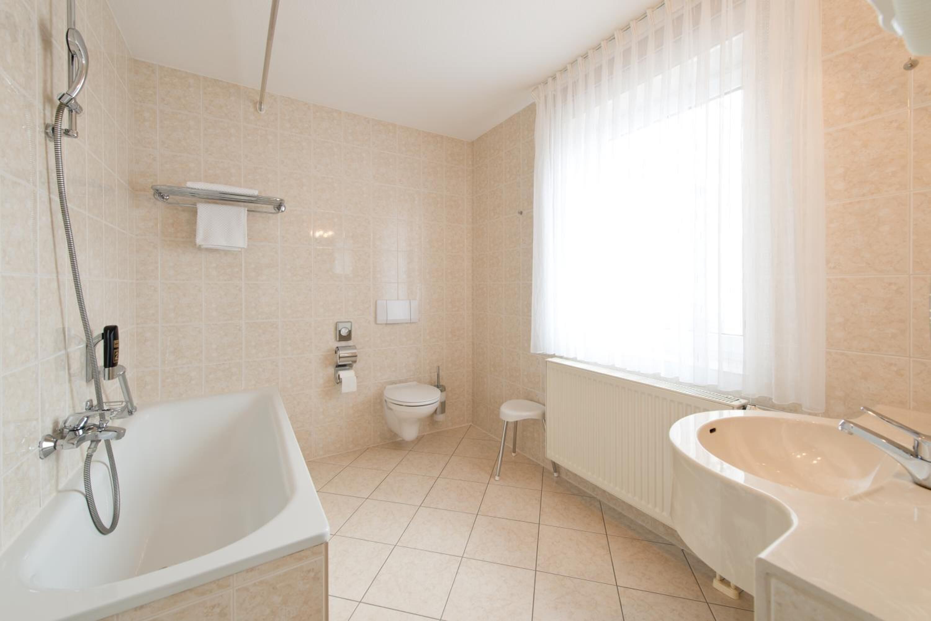 A modern bathroom with a bathtub, a sink, a toilet, and a window with curtains.