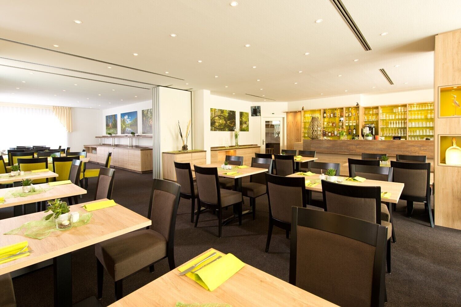 Un restaurante moderno con varias mesas y sillas, una zona de bar con estantes llenos de botellas, y vistas al exterior a través de grandes ventanales.