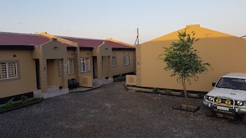 A residential area with beige houses, a gravel driveway, and a parked SUV.
