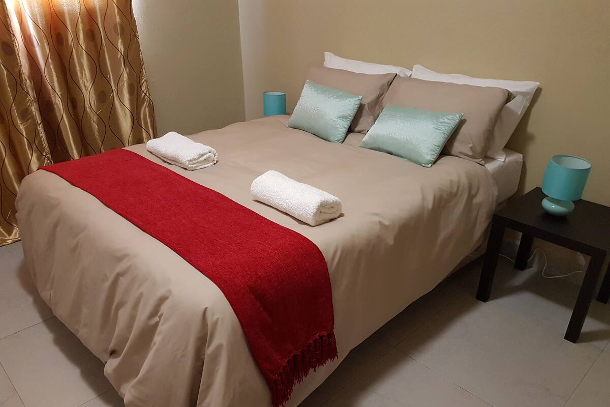 A neatly made bed with a red throw blanket, two pillows, and two bedside lamps on a nightstand.