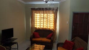 A living room with a sofa, armchairs, a coffee table, and a television. - Sumbulwa Apartments (Livingstone)