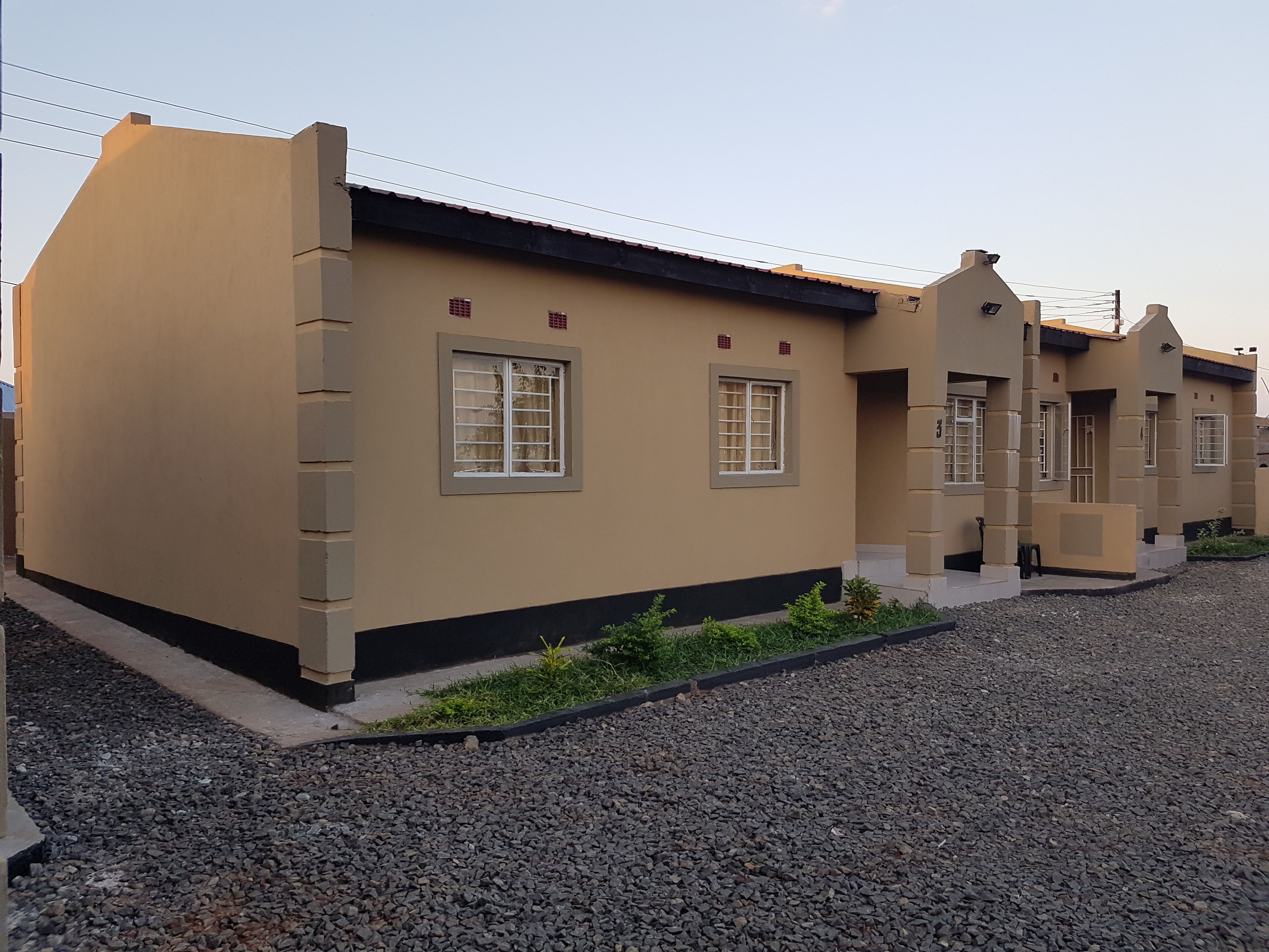 A row of beige buildings with multiple windows and a gravel driveway.