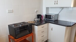 A compact kitchen with white cabinets, a black countertop, a microwave, a toaster, and a small wooden table. - Sumbulwa Apartments (Livingstone)