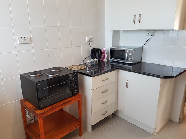 Eine kompakte Küche mit weißen Schränken, einer schwarzen Arbeitsplatte, einer Mikrowelle, einem Toaster und einem kleinen Holztisch.