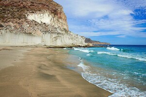 Una playa con arena y un acantilado rocoso.