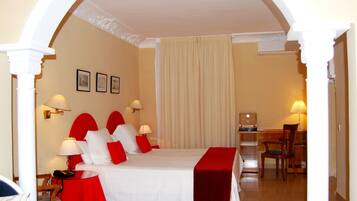 A hotel room with a bed, a desk, and a chair. There are two wall-mounted lamps and a telephone on the desk.