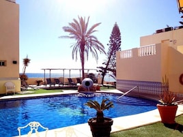 Una piscina con sillas de descanso y palmeras, rodeada de edificios con balcones.