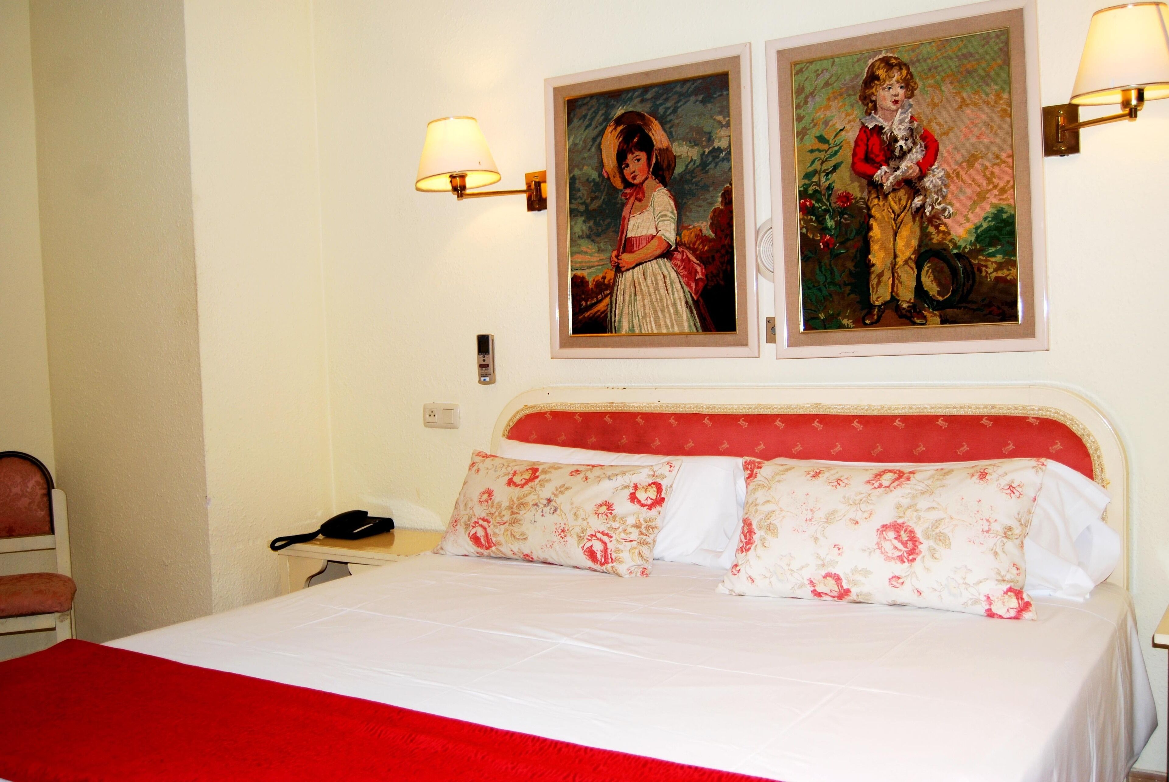 Een hotelkamer met een bed, twee wandlampen en twee ingelijste schilderijen.