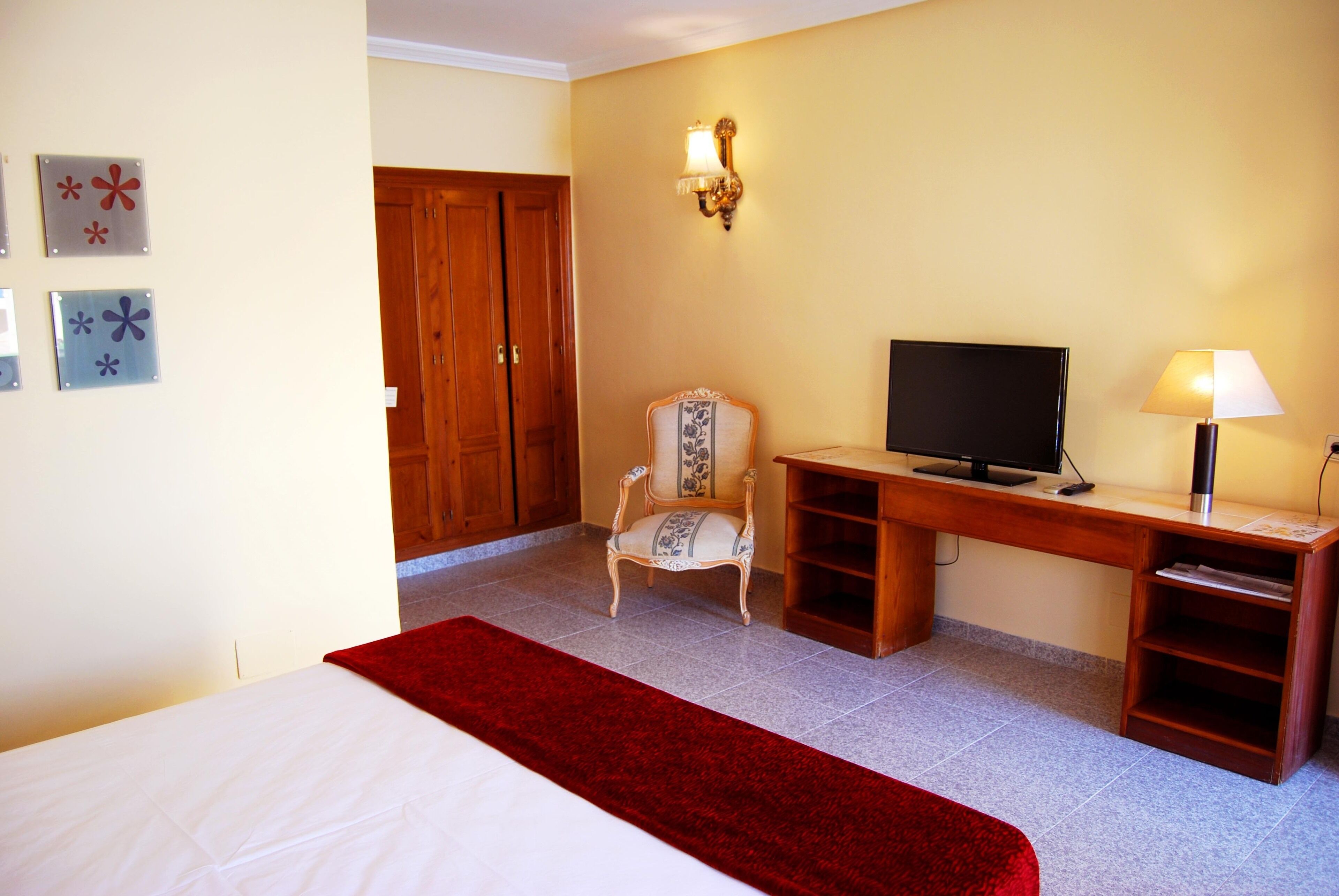 Habitación de hotel con cama, escritorio, televisor, una silla y una manta roja.