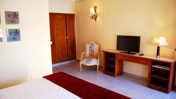 Habitación de hotel con cama, escritorio, televisor, una silla y una manta roja.