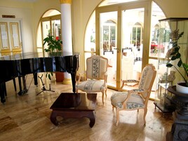 Un piano de cola, dos sillas decorativas y un ventanal de vidrio que da a un espacio exterior con mesas y sillas.