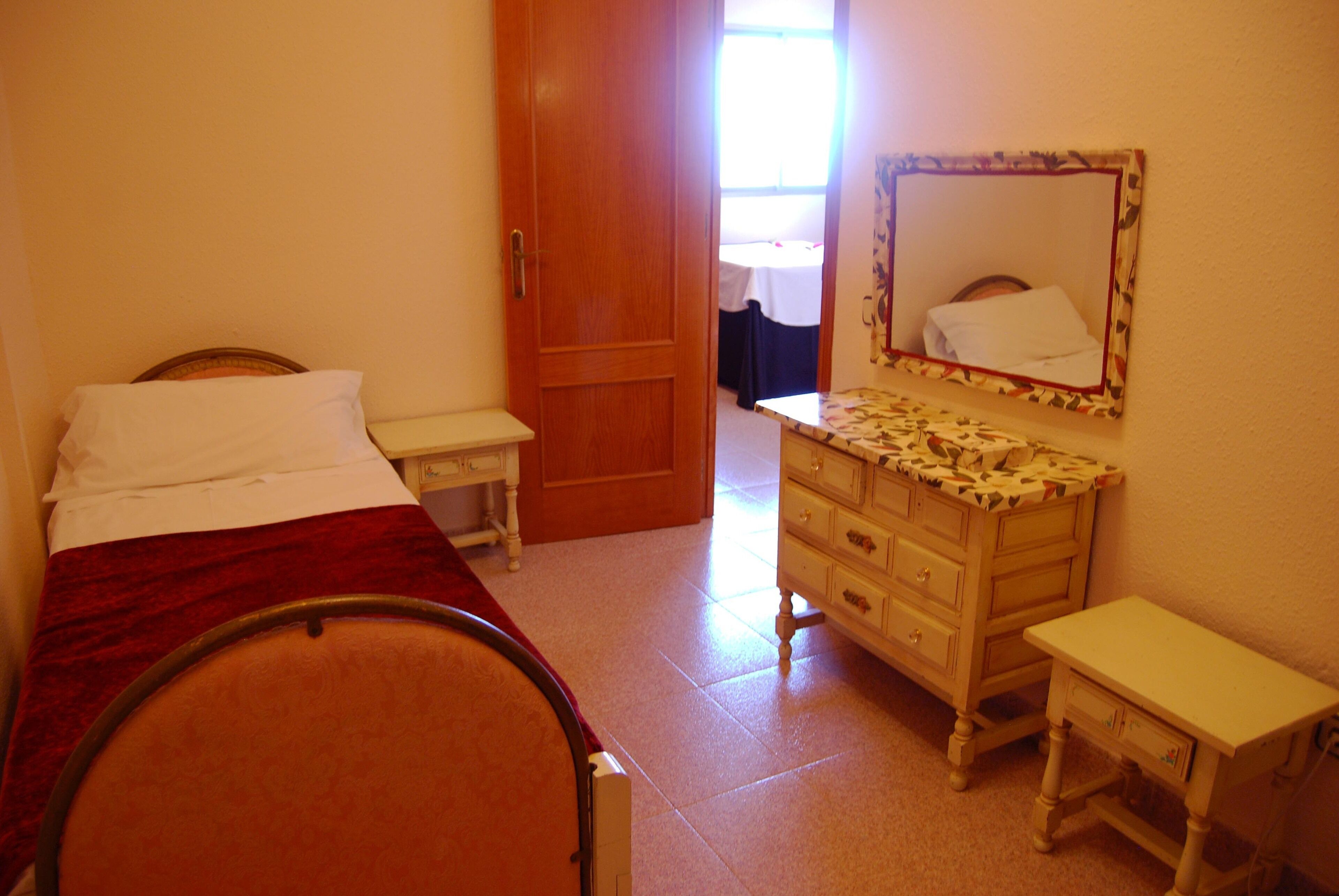 Un dormitorio con cama, cómoda, mesita de noche y una puerta que da a otra habitación.