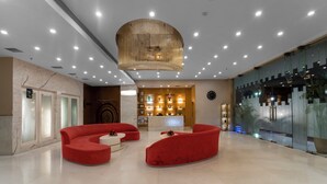 A spacious lobby with a modern design, featuring a large chandelier, red seating area, and a reception desk with a decorative backdrop. - Grand Plaza Jammu (Jammu)