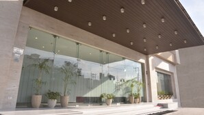 A modern building with large glass windows, a wooden sloped roof, and potted plants in front. - Grand Plaza Jammu (Jammu)