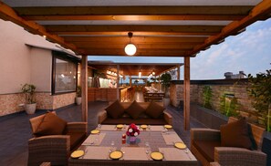 Un patio exterior con mobiliario de mimbre, una mesa de comedor para cuatro personas y una zona de bar al fondo.