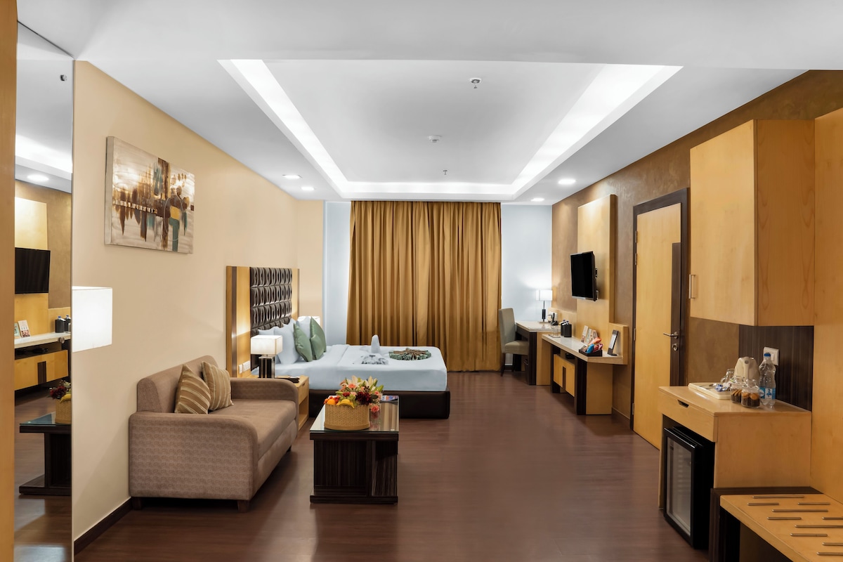 A modern hotel room with a bed, sofa, coffee table, and a desk with a chair.