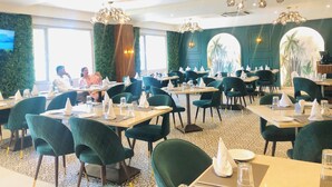 A restaurant with multiple tables and chairs, a green wall with a mural, and a chandelier. - Grand Plaza Jammu (Jammu)