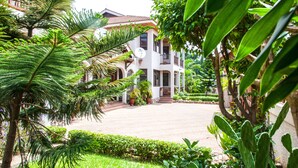 A two-story building with a balcony, surrounded by lush greenery and a paved courtyard. - Mahogany Lodge, Cantonments (Accra)