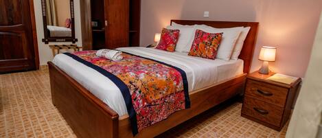 A neatly made bed with a floral bedspread, a wooden nightstand with a lamp, and a wardrobe with a mirror.