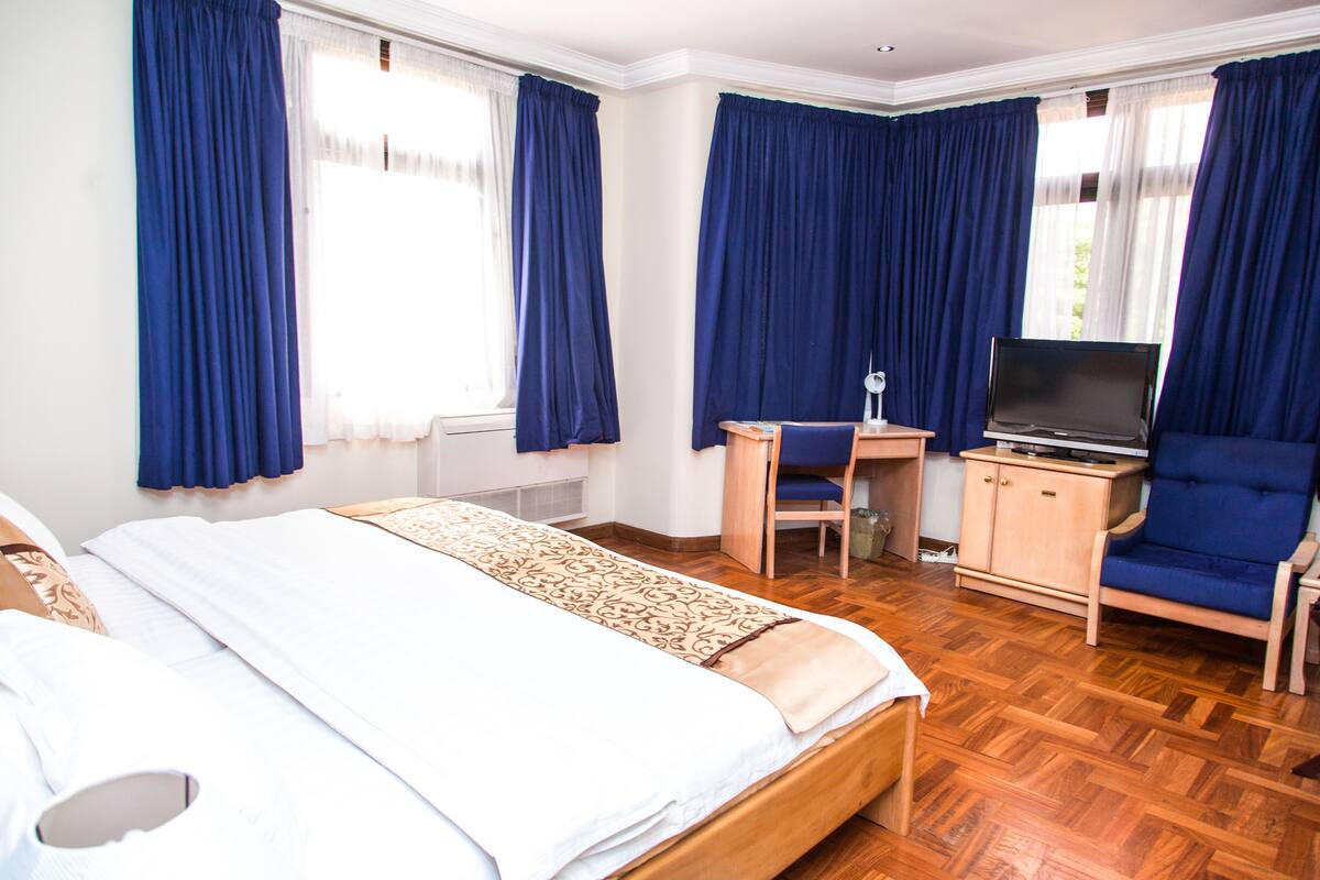 A hotel room with a bed, a desk with a chair, a television, and a cabinet.