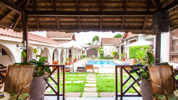 An outdoor pool area with a thatched roof, potted plants, and outdoor seating. - Mahogany Lodge, Cantonments (Accra)