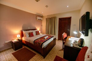 A hotel room with a bed, bedside table, lamp, and a desk with a chair.