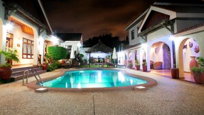 A nighttime swimming pool area with a thatched-roof gazebo, potted plants, and outdoor seating. - Mahogany Lodge, Cantonments (Accra)