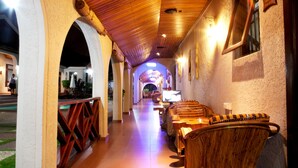 A corridor with wooden ceiling and walls, leading to a seating area with wicker furniture and a television. - Mahogany Lodge, Cantonments (Accra)