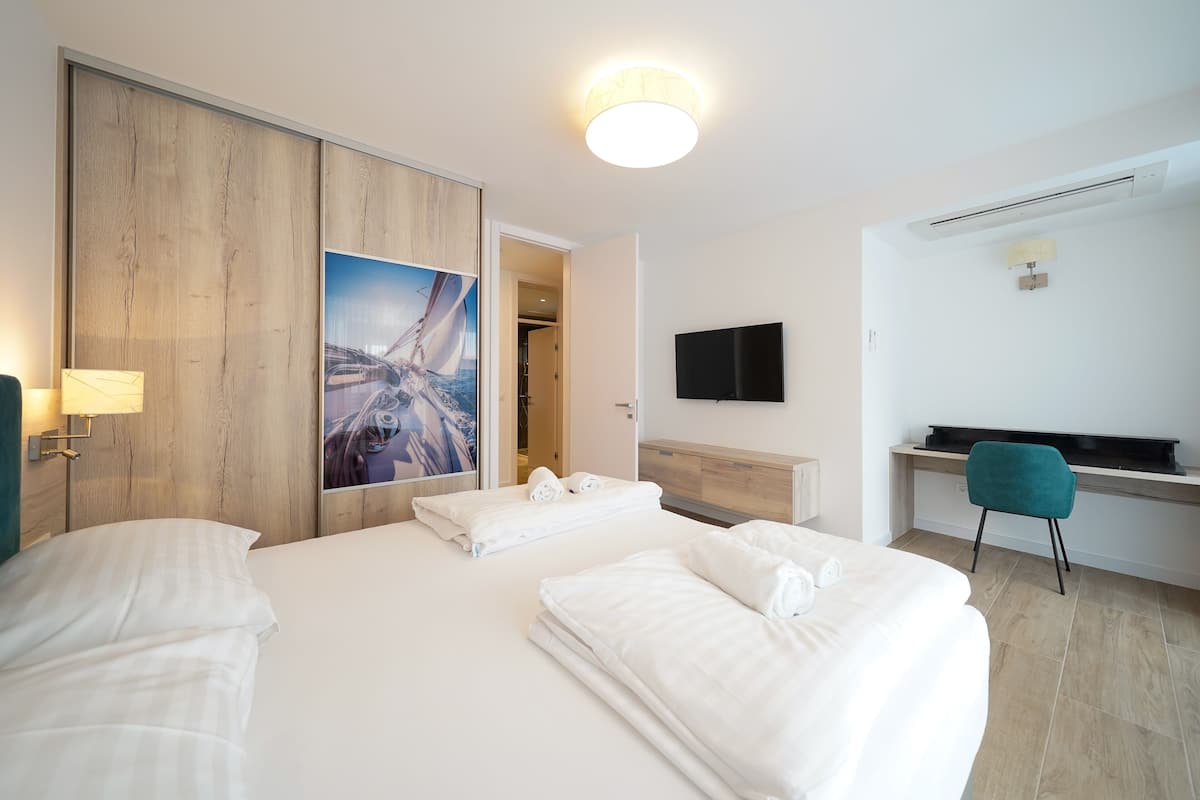 A hotel room with two beds, a desk, a chair, a TV, and a painting on the wall.