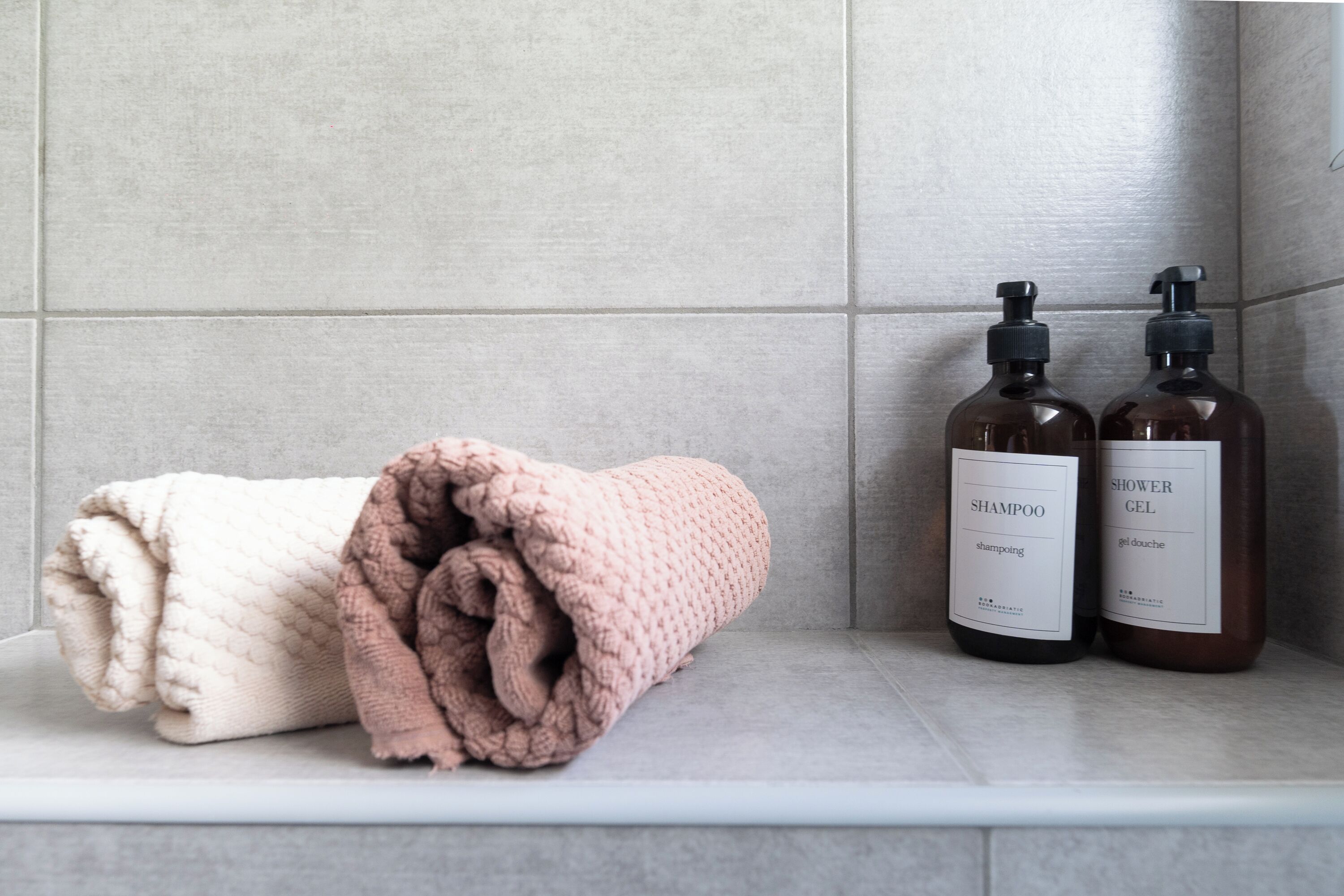 Un estante de baño con dos botellas de champú y gel de ducha, y dos toallas enrolladas.