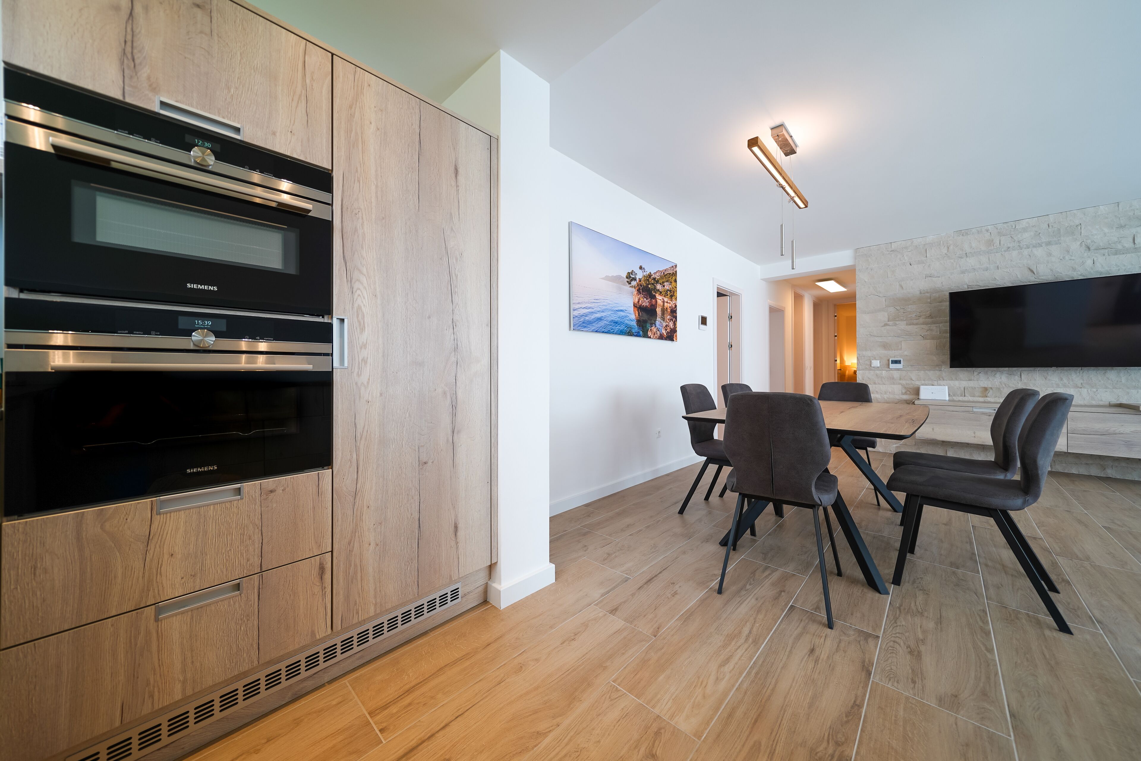 Una cocina moderna con electrodomésticos integrados, un comedor con mesa y sillas, y un televisor montado.
