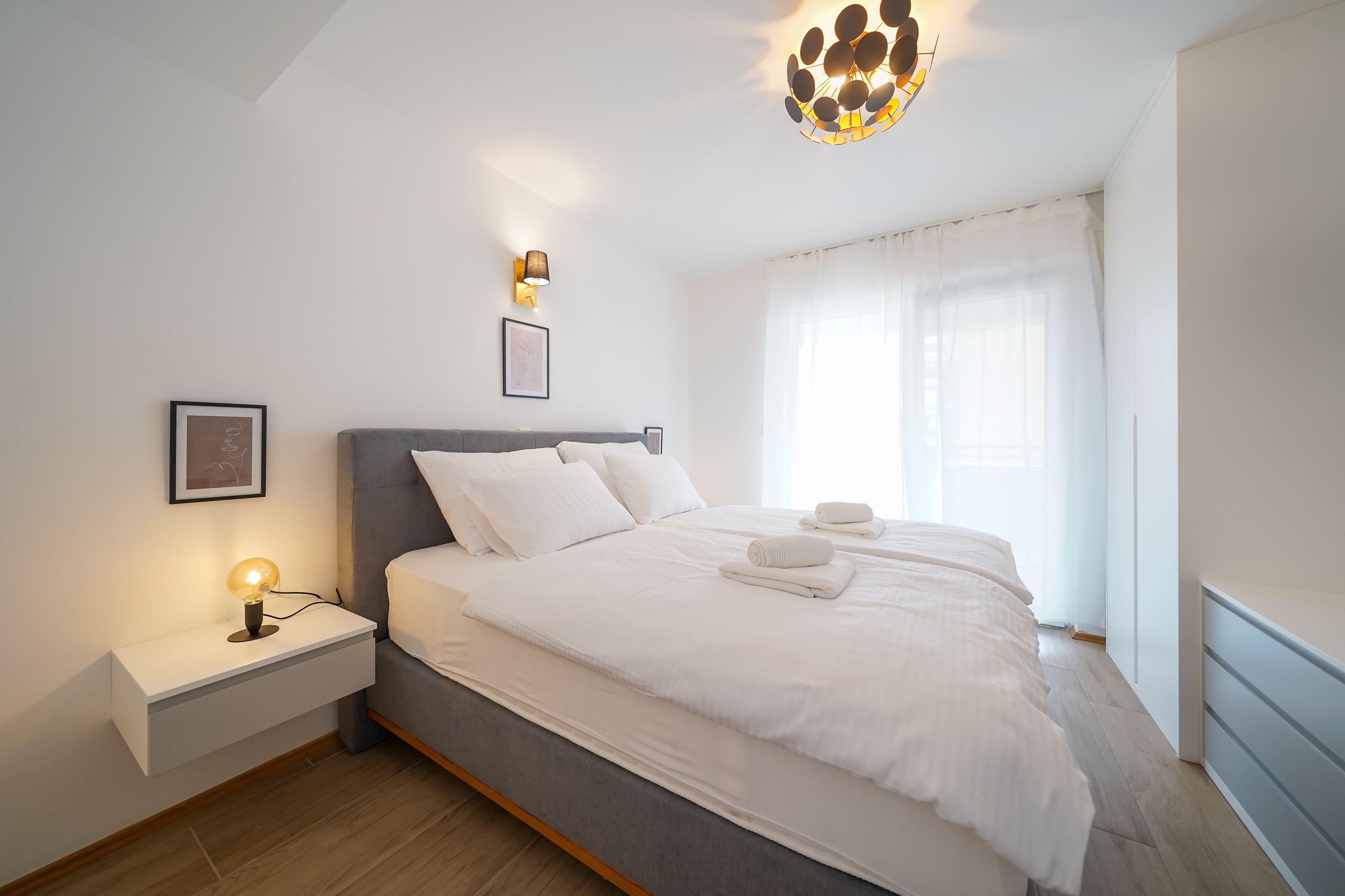 Ein modernes Schlafzimmer mit einem großen Bett, Nachttischen und einer Deckenleuchte.