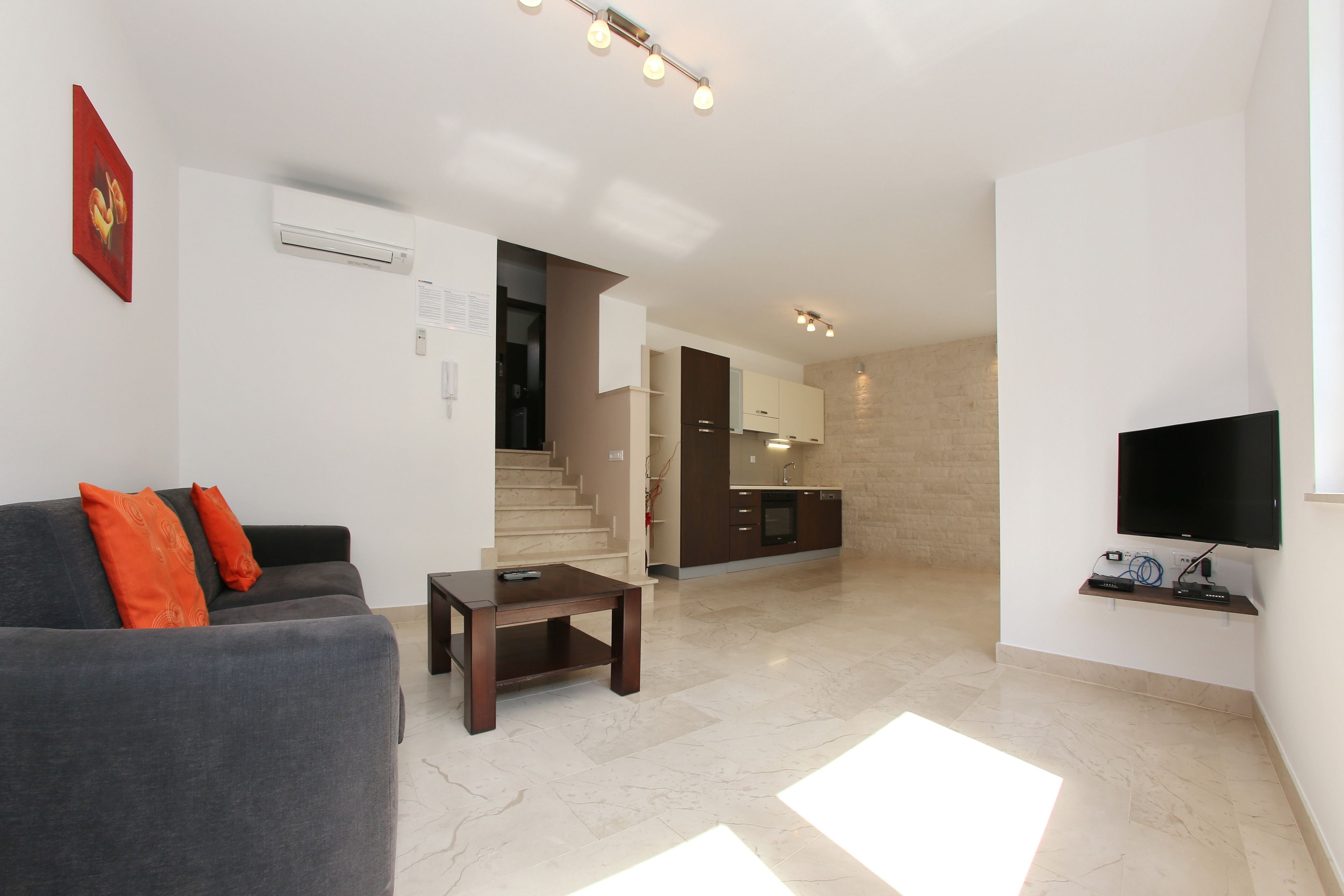 A modern living room with a grey sofa, a small wooden table, and a TV mounted on the wall.