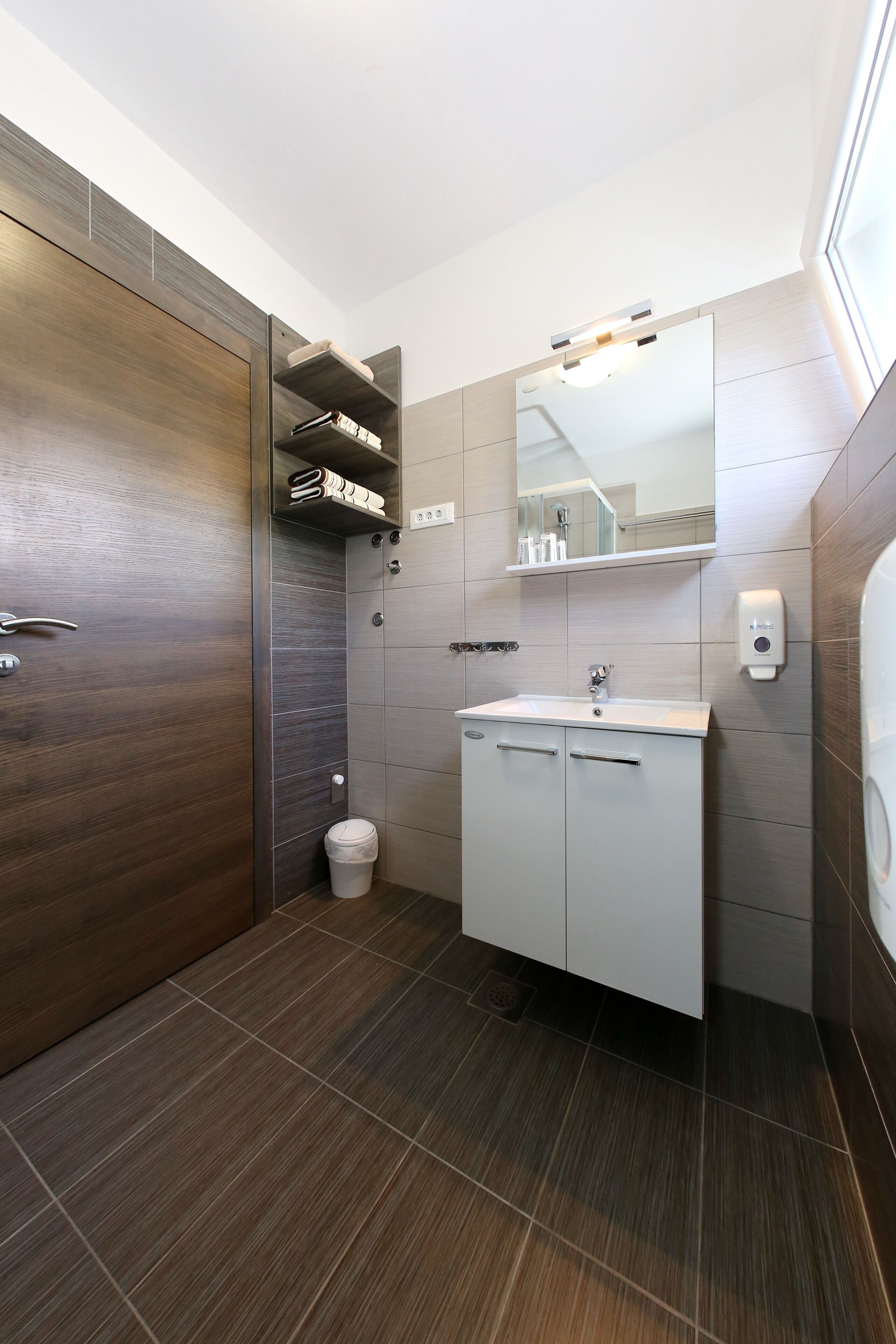 Un bagno moderno con un mobile bagno in legno, uno specchio, un lavandino e una zona doccia.
