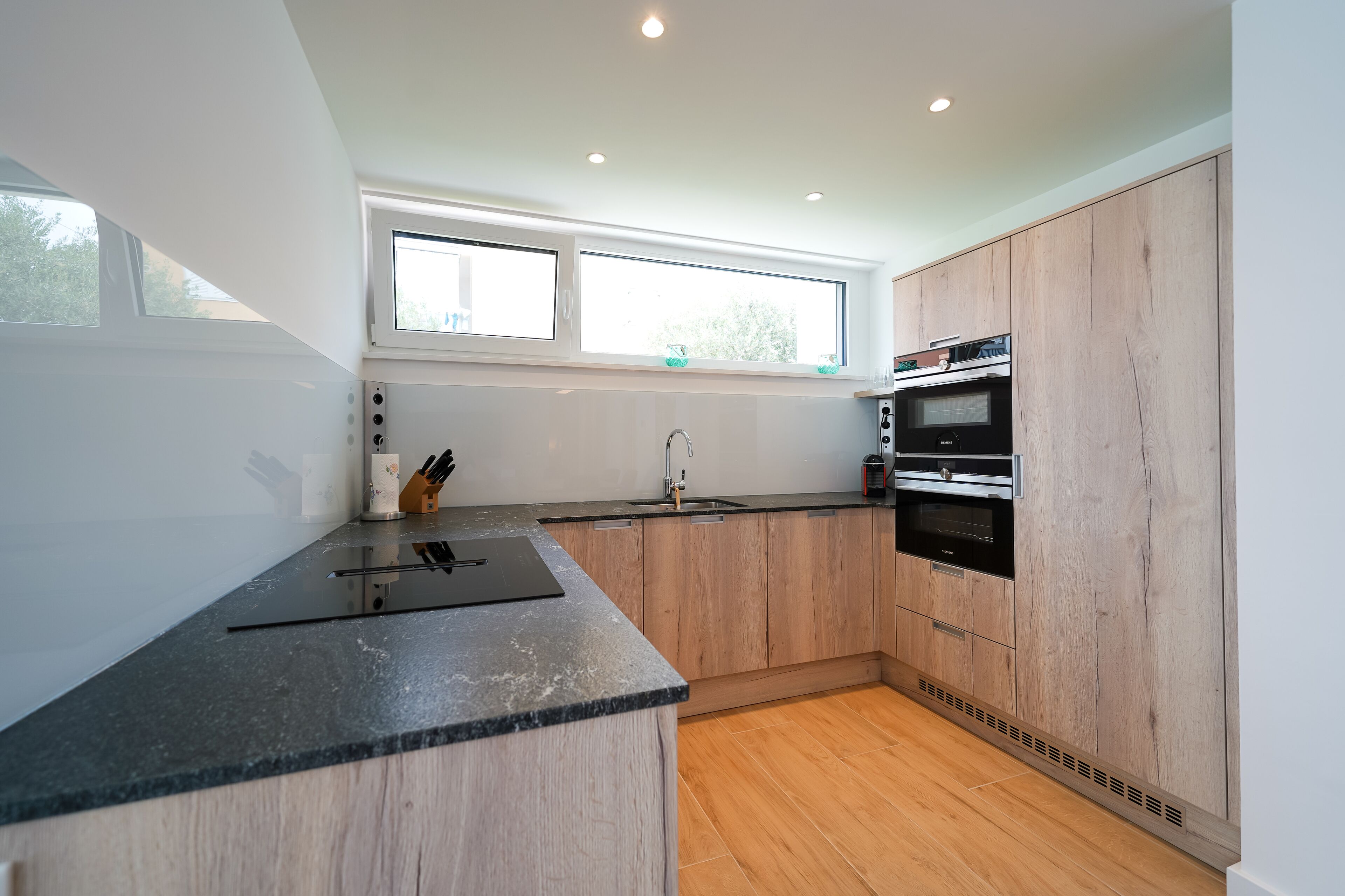 A modern kitchen with wooden cabinets, a black countertop, and a window above the sink.