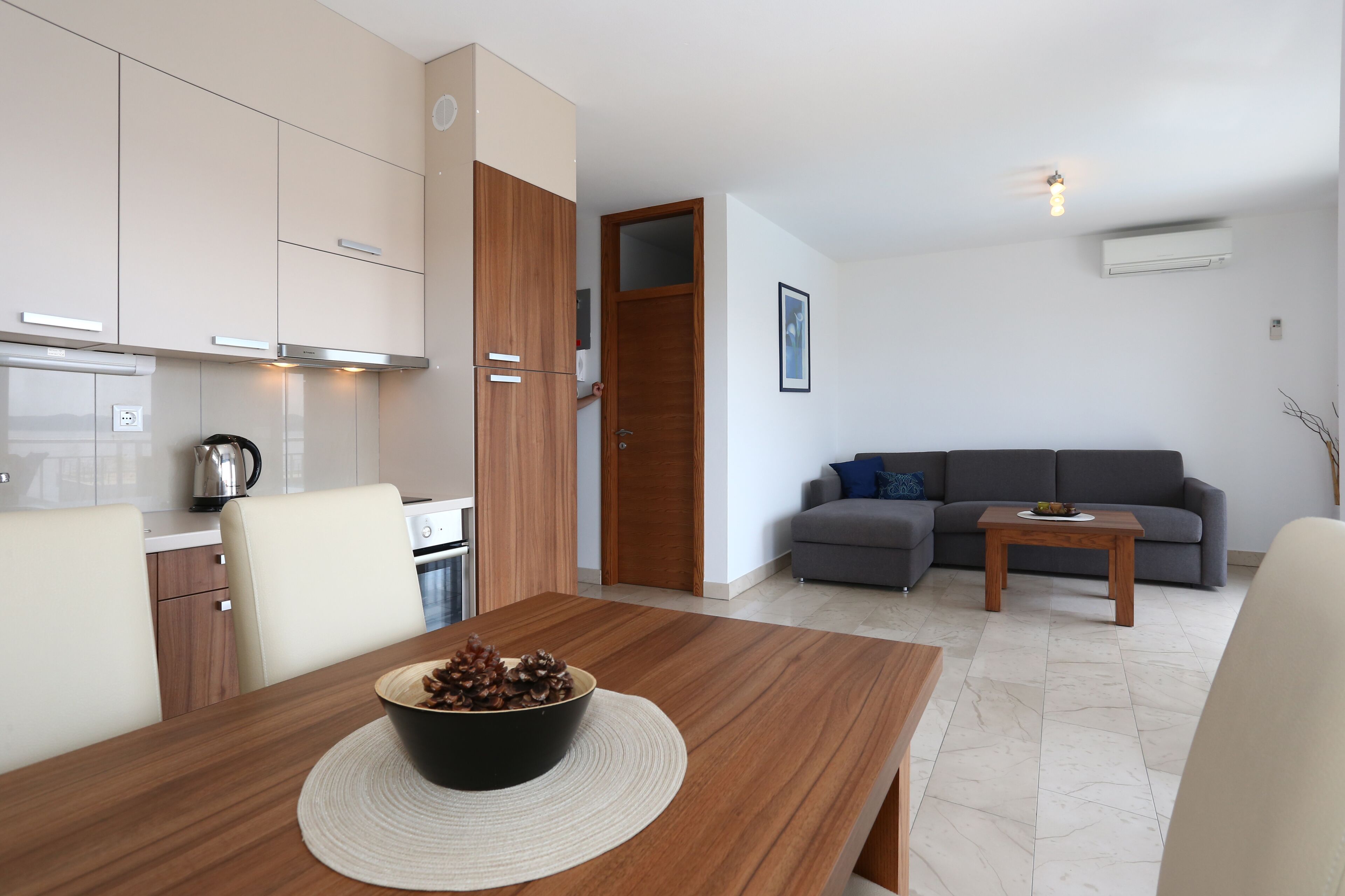 Una sala moderna con un sofá gris, una mesa de centro de madera y una mesa de comedor con un cuenco de piñas.
